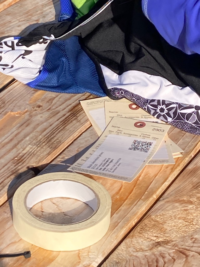 Printed gear tags with QR codes, prices, and seller names on a wooden table